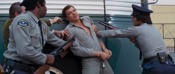 Movie still from “Assault on Precinct 13” (1976), directed by John Carpenter – A group of men holding guns around a man in a gray shirt; Medium shot, Low angle