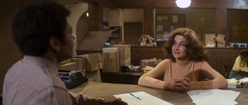 Movie still from “Assault on Precinct 13” (1976), directed by John Carpenter – A woman sitting at a table in front of boxes; Medium shot, Over the shoulder angle