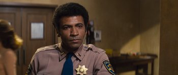 Movie still from “Assault on Precinct 13” (1976), directed by John Carpenter – A man in a police uniform sitting in front of a camera; Close Up shot, Low angle