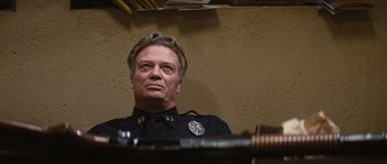 Movie still from “Assault on Precinct 13” (1976), directed by John Carpenter – A man in a police uniform looking up at the ceiling; Close Up shot, Low angle