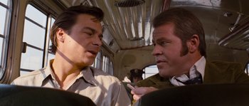 Movie still from “Assault on Precinct 13” (1976), directed by John Carpenter – Two men are talking on a bus while one of them is holding a cell phone in his hand; Close Up shot, Over the shoulder angle