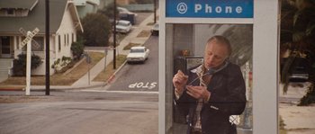 Movie still from “Assault on Precinct 13” (1976), directed by John Carpenter – A man standing in a phone booth looking at his cell phone; Wide shot, High angle