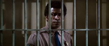 Movie still from “Assault on Precinct 13” (1976), directed by John Carpenter – A man in a police uniform behind a fence; Close Up shot, Low angle