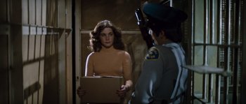 Movie still from “Assault on Precinct 13” (1976), directed by John Carpenter – A woman holding a cardboard box in front of a man; Medium shot, Over the shoulder angle
