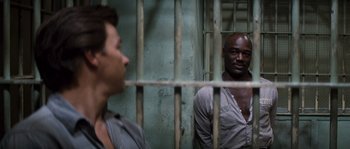 Movie still from “Assault on Precinct 13” (1976), directed by John Carpenter – Two men are standing behind bars in a jail cell; Medium shot, Over the shoulder angle