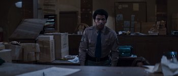 Movie still from “Assault on Precinct 13” (1976), directed by John Carpenter – A man standing in front of a desk in a room; Medium shot, Low angle