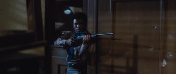 Movie still from “Assault on Precinct 13” (1976), directed by John Carpenter – A man is holding a rifle in a dark room; Medium shot, Low angle