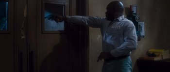 Movie still from “Assault on Precinct 13” (1976), directed by John Carpenter – A man pointing to a picture on a wall; Medium shot, High angle