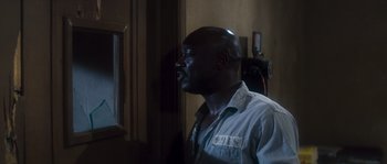 Movie still from “Assault on Precinct 13” (1976), directed by John Carpenter – A man standing next to a window in a room; Medium shot, Over the shoulder angle