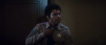 Movie still from “Assault on Precinct 13” (1976), directed by John Carpenter – A police officer adjusting his neck tie while wearing a uniform; Close Up shot, High angle