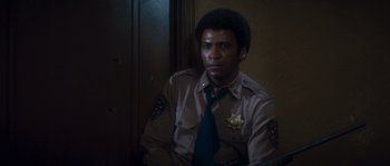 Movie still from “Assault on Precinct 13” (1976), directed by John Carpenter – A man in a police uniform sitting in front of a door; Close Up shot, High angle