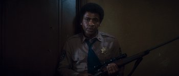 Movie still from “Assault on Precinct 13” (1976), directed by John Carpenter – A man in a uniform holding a gun; Medium shot, High angle