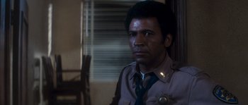 Movie still from “Assault on Precinct 13” (1976), directed by John Carpenter – A man in a police uniform sitting in front of a window; Close Up shot, Low angle