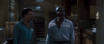 Movie still from “Assault on Precinct 13” (1976), directed by John Carpenter – Two men standing in a dark room looking at something; Medium shot, Low angle