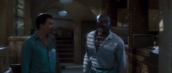 Movie still from “Assault on Precinct 13” (1976), directed by John Carpenter – A man in a prison uniform standing next to another man; Medium shot, Over the shoulder angle