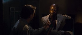Movie still from “Assault on Precinct 13” (1976), directed by John Carpenter – A man is looking into a mirror while another man holds a gun; Medium shot, Over the shoulder angle
