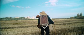 Movie still from “At Eternity's Gate” (2018), directed by Julian Schnabel – A man in a field with a wooden crate on his back; Wide shot, Low angle