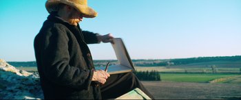 Movie still from “At Eternity's Gate” (2018), directed by Julian Schnabel – An older man sitting on a bench painting a picture; Medium shot, Low angle