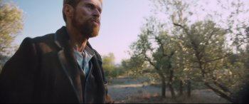 Movie still from “At Eternity's Gate” (2018), directed by Julian Schnabel – A man with a long beard standing next to a tree; Medium shot, Low angle