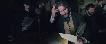 Movie still from “At Eternity's Gate” (2018), directed by Julian Schnabel – A man in a suit and a bow tie is looking at papers; Medium shot, High angle
