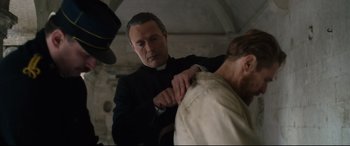 Movie still from “At Eternity's Gate” (2018), directed by Julian Schnabel – A man in a clerical outfit is sewing a shirt; Medium shot, Over the shoulder angle