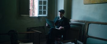 Movie still from “At Eternity's Gate” (2018), directed by Julian Schnabel – A man sitting in a chair with a laptop; Medium shot, Low angle