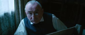 Movie still from “At Eternity's Gate” (2018), directed by Julian Schnabel – An older man in a vest and tie looking at a laptop; Close Up shot, Low angle