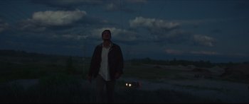 Movie still from “At First Light” (2018), directed by Jason Stone – A man standing next to a car on a road; Wide shot, Low angle
