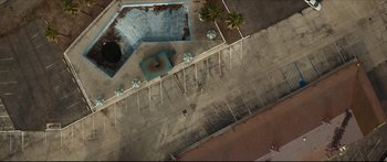 Movie still from “At First Light” (2018), directed by Jason Stone – An aerial view of a swimming pool with a lot of tables and chairs; Extreme Wide shot, Overhead angle