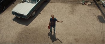 Movie still from “At First Light” (2018), directed by Jason Stone – A man standing on the side of the road holding a cell phone; Wide shot, Overhead angle