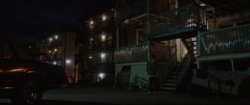 Movie still from “At First Light” (2018), directed by Jason Stone – A person standing in front of a building at night; Extreme Wide shot, Low angle