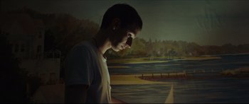 Movie still from “At First Light” (2018), directed by Jason Stone – A man standing in front of a painting of a lake; Medium shot, Low angle