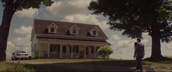 Movie still from “At First Light” (2018), directed by Jason Stone – A house sitting on top of a grass covered hill; Extreme Wide shot, Low angle