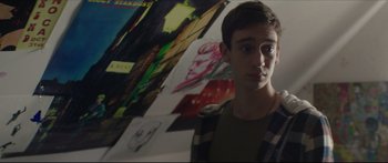 Movie still from “At First Light” (2018), directed by Jason Stone – A young man standing in front of a wall covered in pictures; Close Up shot, Over the shoulder angle