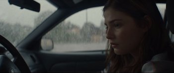 Movie still from “At First Light” (2018), directed by Jason Stone – A woman sitting in the driver's seat of a car looking out the window; Close Up shot, Over the shoulder angle