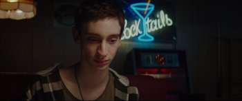 Movie still from “At First Light” (2018), directed by Jason Stone – A young man in front of a cocktail sign; Close Up shot, Over the shoulder angle