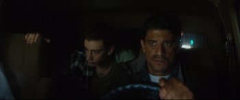 Movie still from “At First Light” (2018), directed by Jason Stone – Two men sitting in a car looking at the camera; Close Up shot, Over the shoulder angle