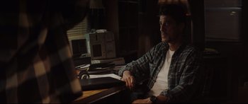 Movie still from “At First Light” (2018), directed by Jason Stone – A man sitting at a table in front of a computer; Medium shot, Over the shoulder angle