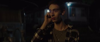 Movie still from “At First Light” (2018), directed by Jason Stone – A young man talking on a cell phone in the dark; Close Up shot, Over the shoulder angle