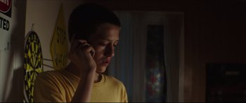 Movie still from “At First Light” (2018), directed by Jason Stone – A young man talking on a cell phone in a dark room; Close Up shot, Low angle