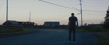 Movie still from “At First Light” (2018), directed by Jason Stone – A man standing on the side of a road; Wide shot, Low angle