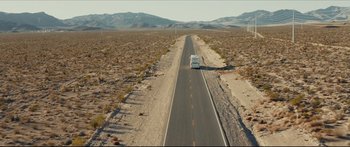 Movie still from “At First Light” (2018), directed by Jason Stone – An rv driving down a desert road in the middle of the day; Extreme Wide shot, High angle