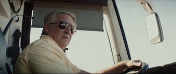 Movie still from “At First Light” (2018), directed by Jason Stone – An older man driving a car wearing sunglasses; Close Up shot, Low angle