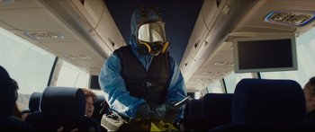 Movie still from “At First Light” (2018), directed by Jason Stone – A man in a hazmat suit and a gas mask on a plane; Medium shot, Low angle