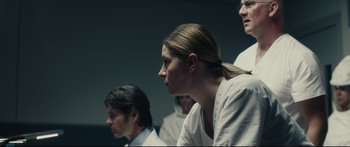 Movie still from “At First Light” (2018), directed by Jason Stone – Three people are sitting in a room and one of them is wearing a white shirt; Close Up shot, Over the shoulder angle