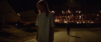 Movie still from “At First Light” (2018), directed by Jason Stone – A woman in a white shirt is walking down the street; Wide shot, Low angle
