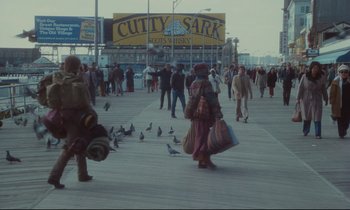 Movie still from “Atlantic City” (1980), directed by Louis Malle – A crowd of people walking on a boardwalk near the water; Wide shot, Over the shoulder angle