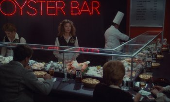 Movie still from “Atlantic City” (1980), directed by Louis Malle – A woman standing in front of a counter with food on top of it; Wide shot, Over the shoulder angle