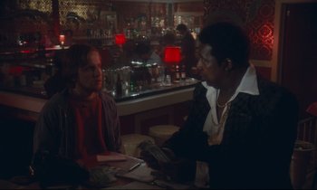 Movie still from “Atlantic City” (1980), directed by Louis Malle – Two people sitting at a table in front of a bar; Medium shot, Over the shoulder angle