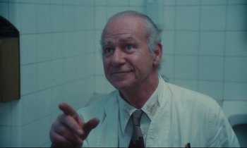 Movie still from “Atlantic City” (1980), directed by Louis Malle – An older man wearing a white lab coat and a tie; Close Up shot, Low angle